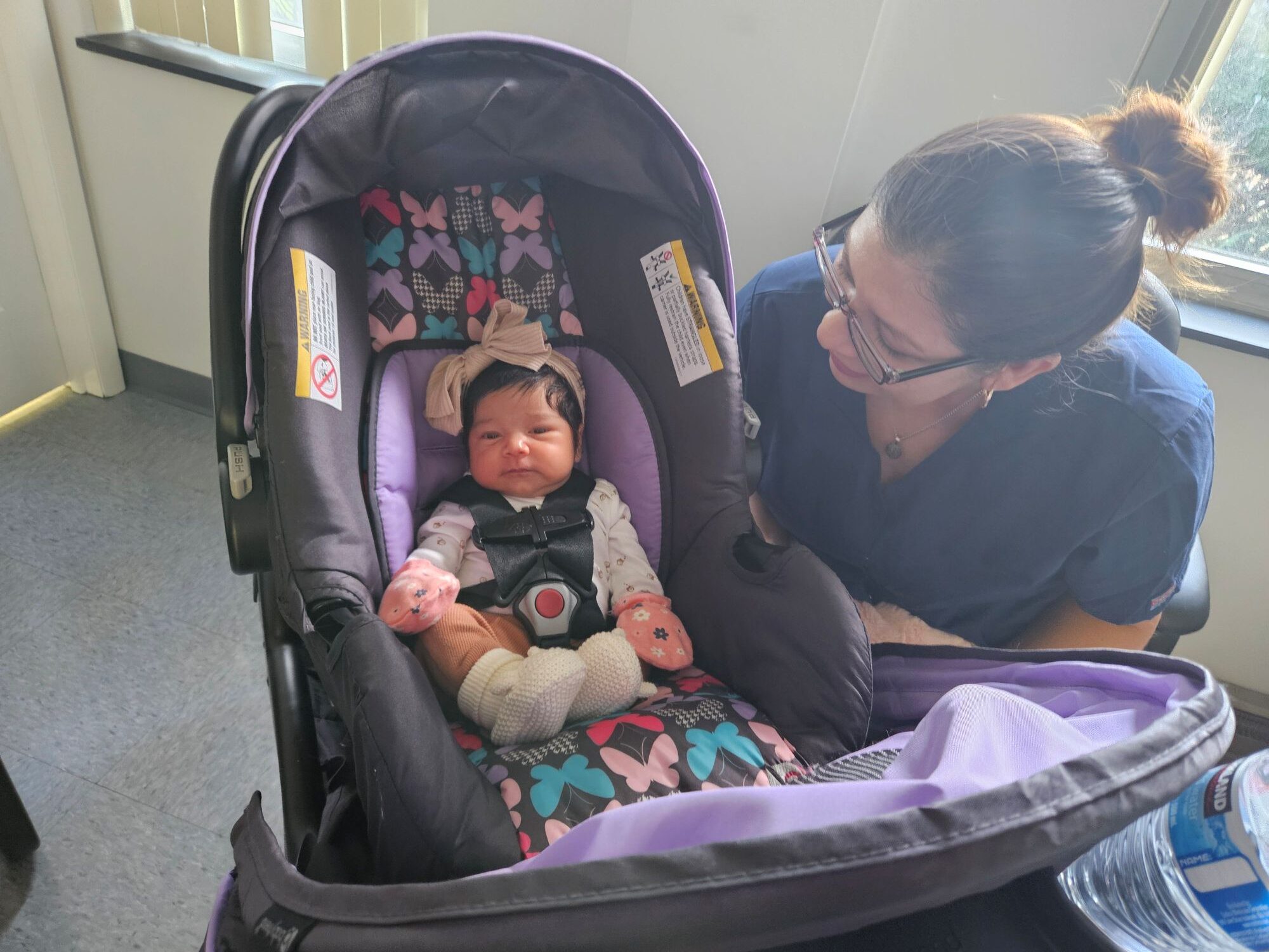 A young baby sits in a car seat in the office as a Bright Hope staff member looks at her.
